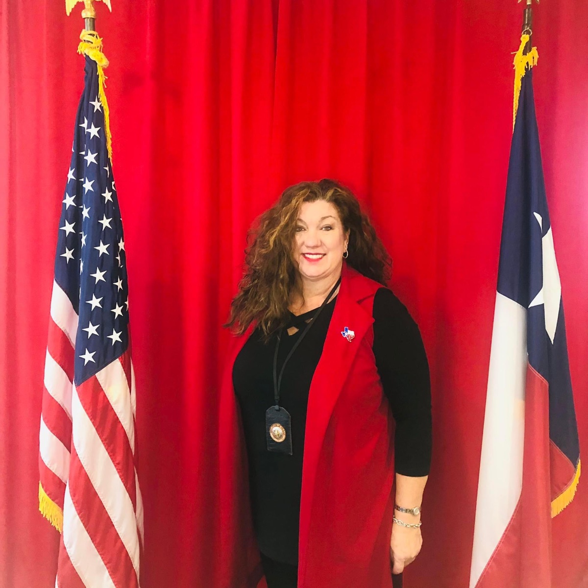 Audrey Young standing between the United States and Texas flags in a red vest